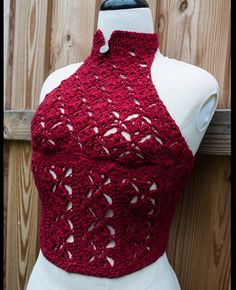 a mannequin wearing a red crochet top on a wooden fence background