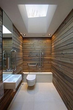 a modern bathroom with wood paneling and skylights above the toilet, sink and bathtub