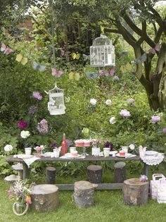 an outdoor table with birdcages and flowers in the background, surrounded by greenery