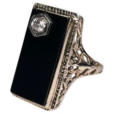 This is an Art Deco 14K white gold, diamond and onyx cocktail ring. It depicts a rectangular black onyx top in white gold bezel setting. The onyx has a reeded gold frame. A round cut diamond on prong setting embellishes one of the corner of the onyx. Each shank of the ring is adorned with a reticulated work made of leaves and hearts. The onyx stone symbolizes courage, power and good fortune. Rectangular Onyx Ring For Formal Occasions, Formal Rectangular Onyx Ring, Black Art Deco Diamond Ring, Formal Black Jewelry With Rectangular Stone, Elegant Rectangular Diamond Ring With Polished Finish, Vintage Onyx Ring, Onyx Rings, No Ordinary Girl, Gold Pinky Ring