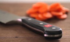 a knife sitting on top of a wooden table next to carrots