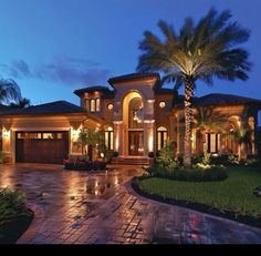 a large house with palm trees in the front yard and lights on it's windows