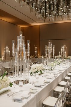 a long table is set with clear vases and white flowers in the centerpieces