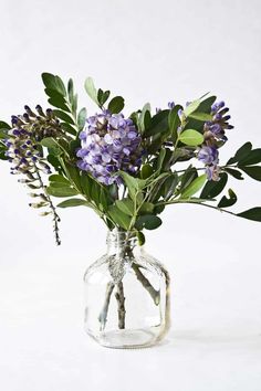 a glass vase filled with purple flowers and greenery