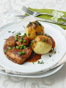 a white plate topped with meat covered in gravy and peas next to a fork