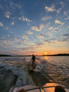 a person on a surfboard riding in the water at sunset with another person behind him