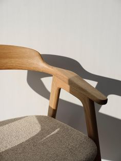 a wooden chair sitting in front of a white wall with the shadow of a person's arm on it