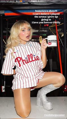 a woman sitting on the ground with her legs crossed and holding a coffee mug in one hand