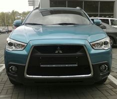 the front end of a blue car parked in a parking lot next to other cars