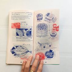 a hand holding an open book on top of a white table with red and blue designs