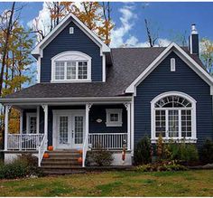 a blue house with white trim and windows on the front porch is surrounded by trees