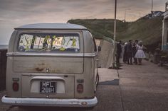 an old vw bus parked on the side of the road with people standing around