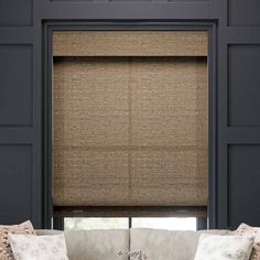 a living room with a couch and window covered in brown roman blind shades on the windowsill