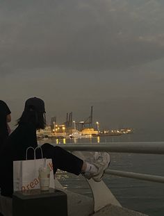 two people sitting on a ledge looking out at the water and buildings in the distance