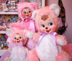 three pink teddy bears sitting next to each other on a bed in a room full of toys