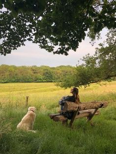 a woman sitting on a wooden bench next to a white dog in a grassy field