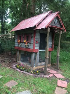 a small chicken coop in the middle of a grassy area with flowers growing on it