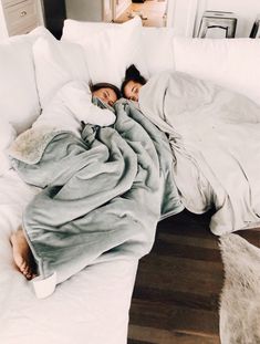 two people sleeping on a couch covered in blankets