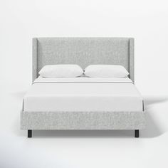 an upholstered bed with white linens and pillows on it, against a wall