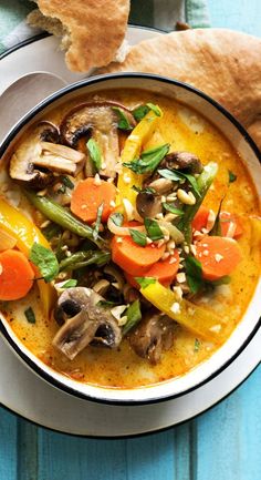 a bowl of soup with carrots, mushrooms and other vegetables on a blue table