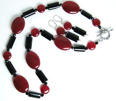 Red mountain jade, black tourmaline necklace (19 inches) with a sterling silver toggle clasp. The matching earrings are on sterling silver leverbacks with a 1.4-inch drop. Red mountain jade is a gemstone of color-enhanced high-grade dolomite marble from Asia. Both red mountain jade and tourmaline are gemstones. There are two shapes of red mountain jade beads: flattened ovals (25 x 18 mm) and flattened round beads (11 mm in diameter).The black tourmaline beads are flattened cylinders (16 x 9 mm).There are also 4 mm black faceted beads in the necklace. Red mountain jade is the gemstone of October-November. Tourmaline is a birthstone of October. Elegant Jade Round Beads Jewelry, Elegant Jade Jewelry With Round Beads, Elegant Jade Beaded Jewelry, Classic Jade Gemstone Beads Jewelry, Round Onyx Gemstone Beads Jewelry, Sterling Silver Costume Jewelry Gift, Costume Jewelry In Sterling Silver For Gifts, Black Agate Round Bead Jewelry, Black Agate Round Beads Jewelry