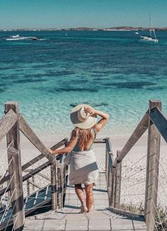 a woman wearing a straw hat walking down stairs to the beach