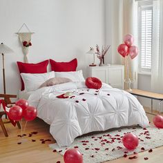 a bedroom decorated in white and red for valentine's day with rose petals on the bed