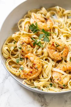 pasta with shrimp and parsley in a white bowl on a marble countertop, ready to be eaten