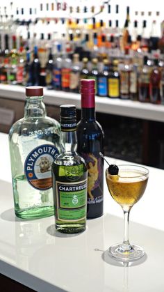 bottles of alcohol sit on a bar next to a glass with an olive in it