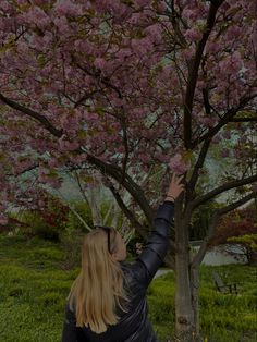 a woman reaching up to a tree with pink flowers