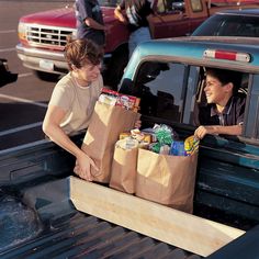 two people in the back of a pickup truck with bags full of food and snacks