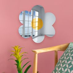 a pink wall with a flower shaped mirror on it and a plant in the foreground