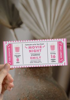 a person holding up a pink and white ticket for a movie night with the date on it