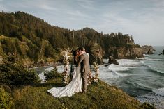 a bride and groom standing on the edge of a cliff overlooking the ocean