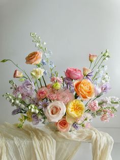 a vase filled with lots of colorful flowers on top of a white cloth covered table