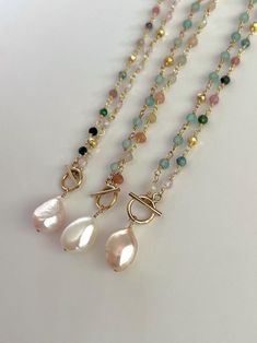 three different necklaces with pearls and beads on white table top next to each other