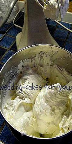 a metal bowl filled with white frosting on top of a blue tile counter next to a mixer