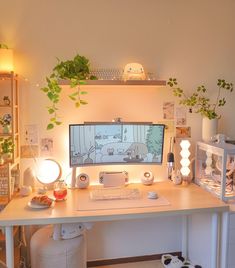 a white desk with a computer on it and some plants in front of the monitor