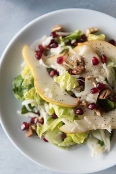 a white plate topped with an apple and salad covered in cheese dressing, pomegranates and nuts