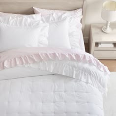 a white bed with pink ruffles and pillows on top of the comforter