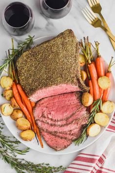 a white plate topped with roast beef and carrots next to two glasses of wine