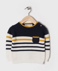 a sweater hanging on a hanger with a white and yellow striped shirt in the background