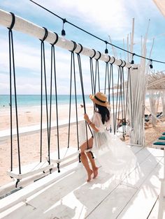 a woman in a straw hat is sitting on a hammock at the beach