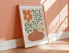 an orange vase with flowers is on the floor next to a framed art print against a peach wall