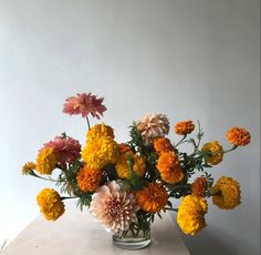 a vase filled with lots of different colored flowers on top of a wooden table next to a white wall