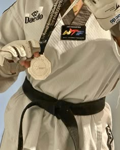 a man wearing a white uniform and black belt holding a silver medal in his right hand