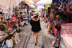 a woman walking through an open market with lots of umbrellas hanging from the ceiling