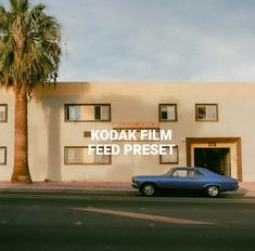 a blue car is parked in front of a building with palm trees on the side