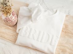 a white t - shirt with the word bride on it next to a flower vase