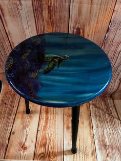 a blue table with a turtle painted on it's side sitting against a wooden wall